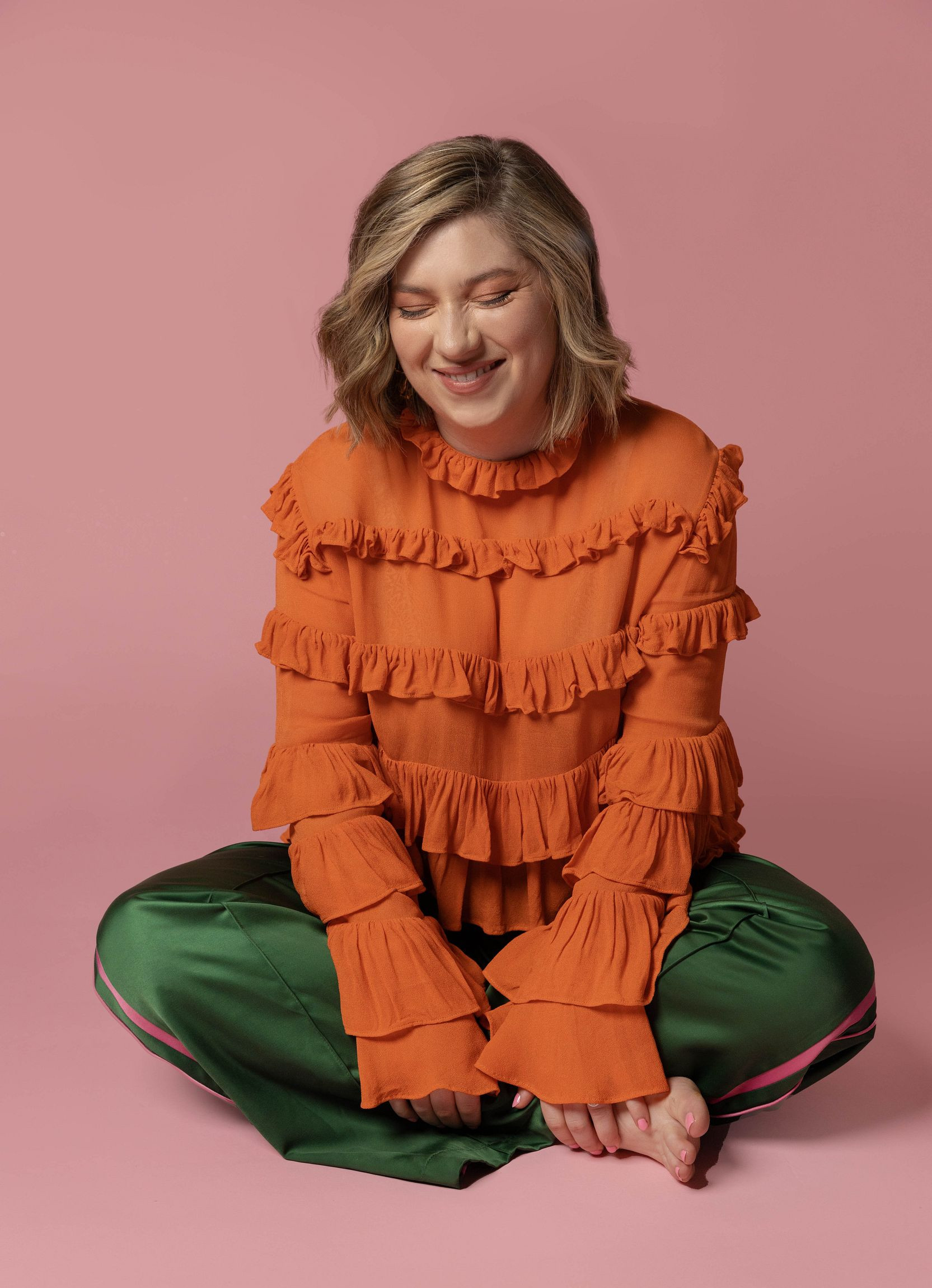 Harriett in an orange shirt, sitting crossed legged, laughing