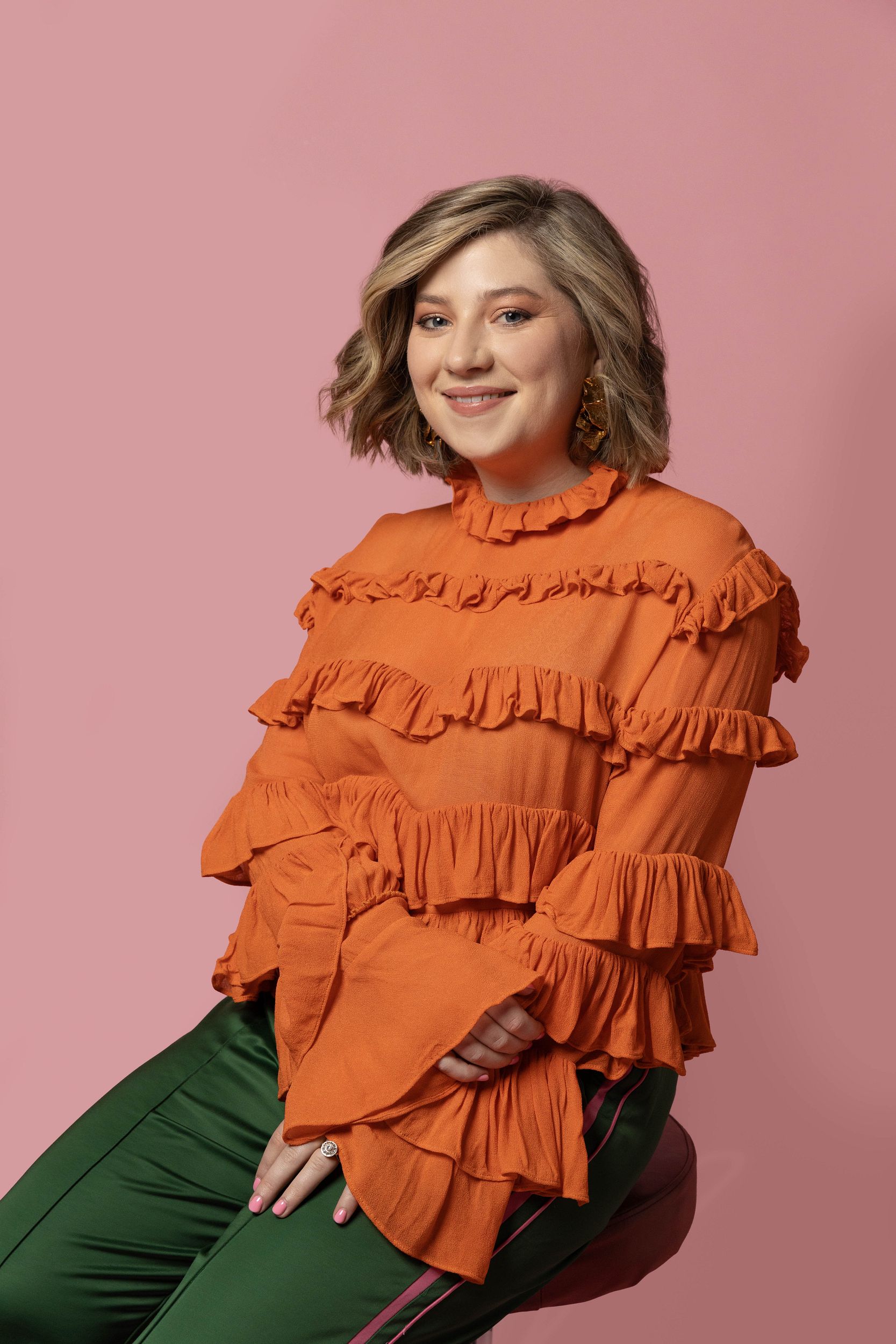 Harriett in an orange shirt, sitting on a stool, smiling